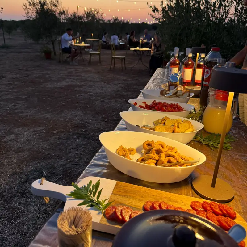 L'aperitivo apparecchiato tra gli ulivi al tramonto: taralli, salumi, pomodori e vini della tenuta